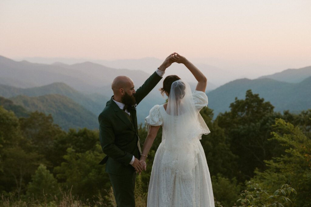 Man spinning woman in front of mountains at sunset on their wedding day.