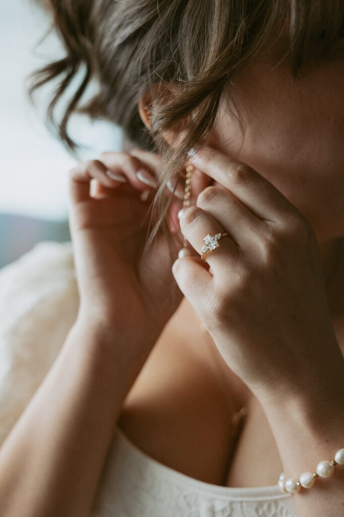 Close up of a woman putting in her earring on her wedding day with her engagement ring showing. 