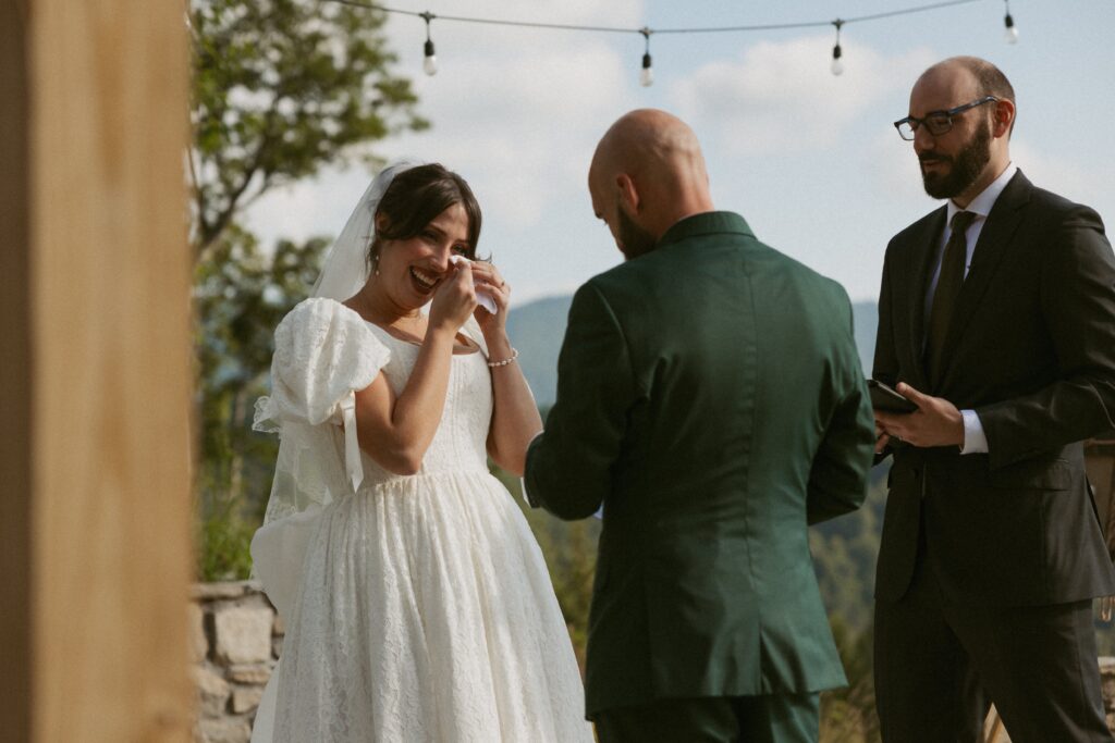 Woman wiping tears away as man reads his vows to her during their wedding ceremony.