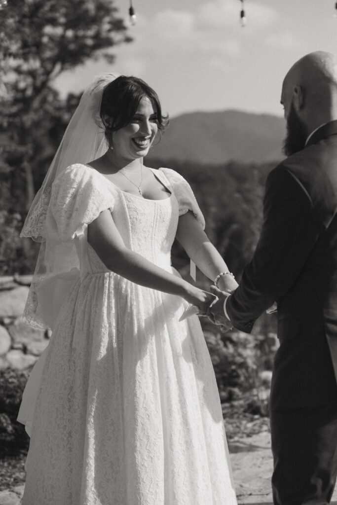 Man and woman holding hands and smiling at each other during wedding ceremony. 