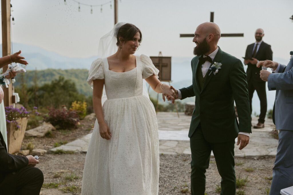 Man and woman walking back down wedding aisle after getting married holding hands and smiling at each other. 