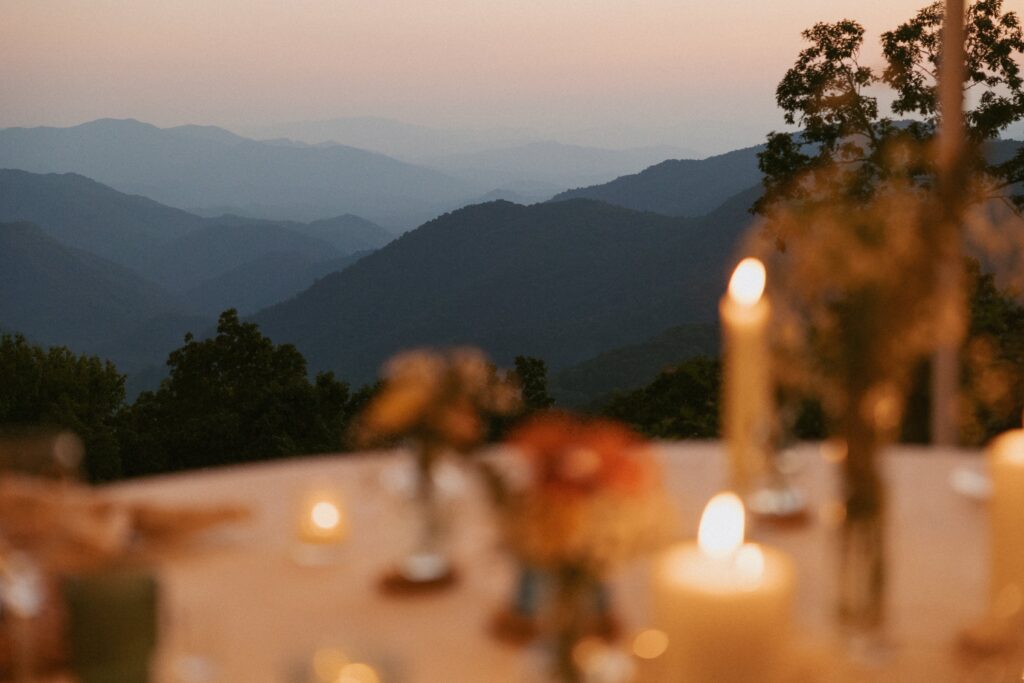 Close up of candles and flowers on a table with the mountains in the background in focus. 