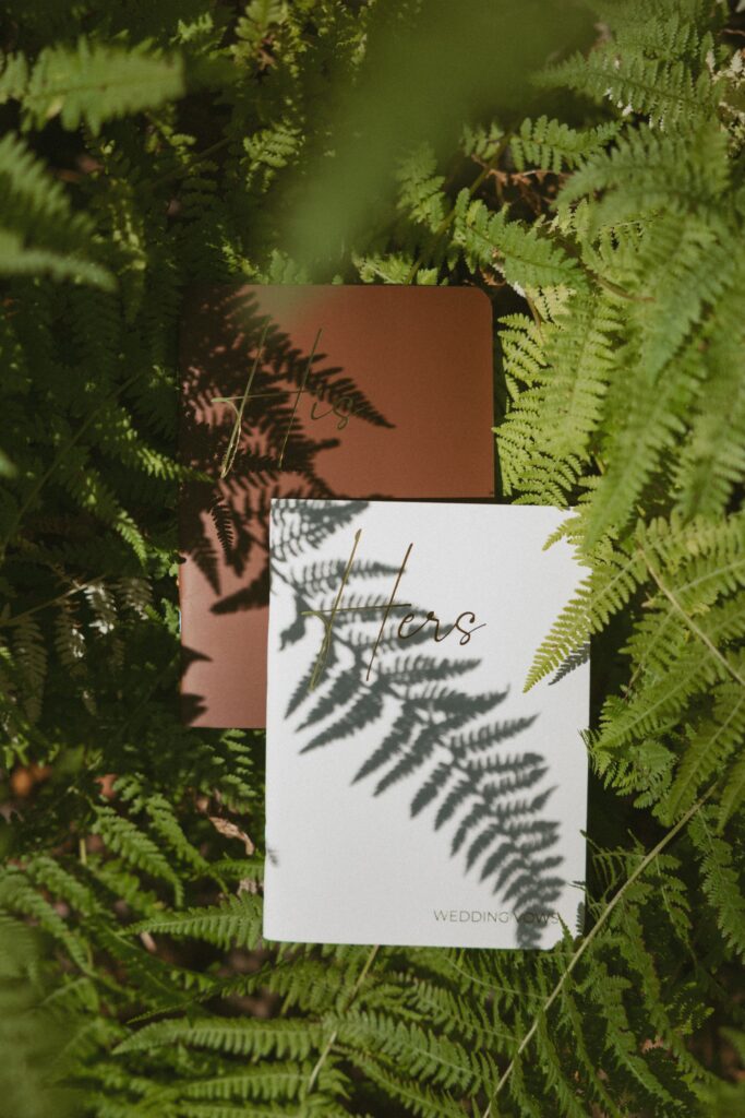 His and hers vow books laying in a bed of ferns.