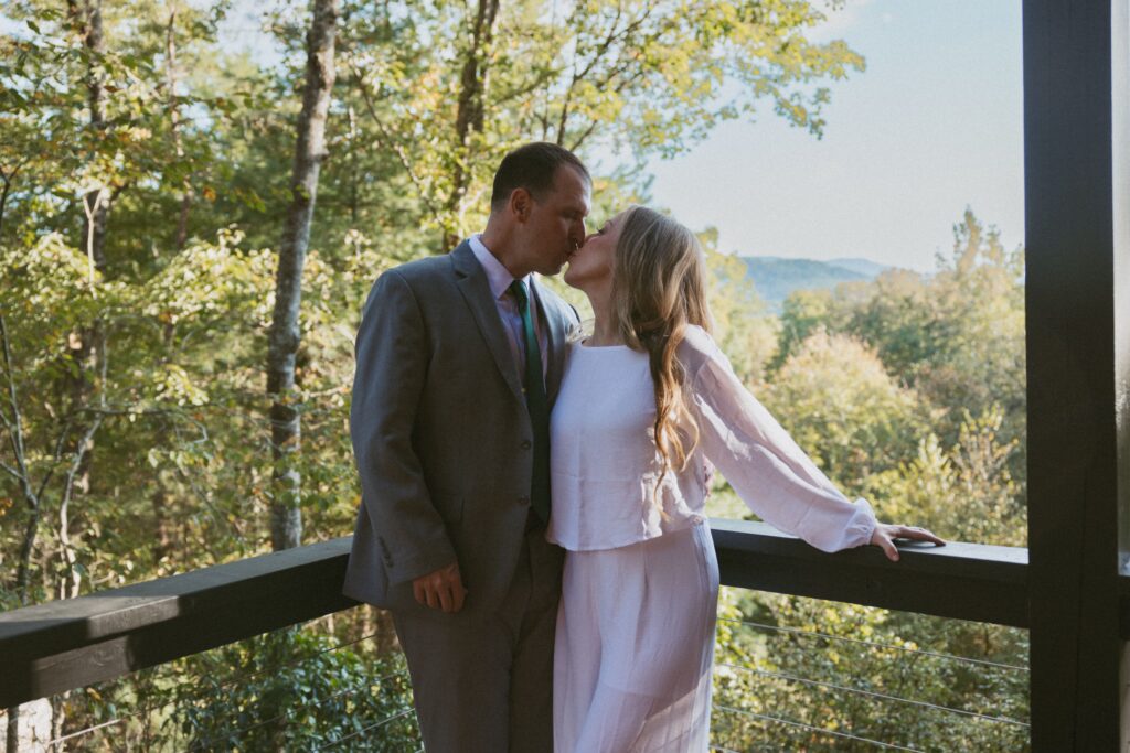 Man and woman kissing on deck of airbnb with mountains behind them.