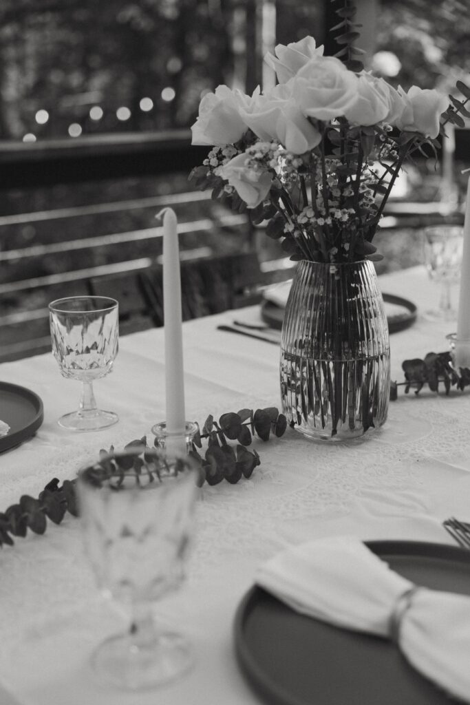 Roses, drinking glasses, plates, and candles on a table scape.