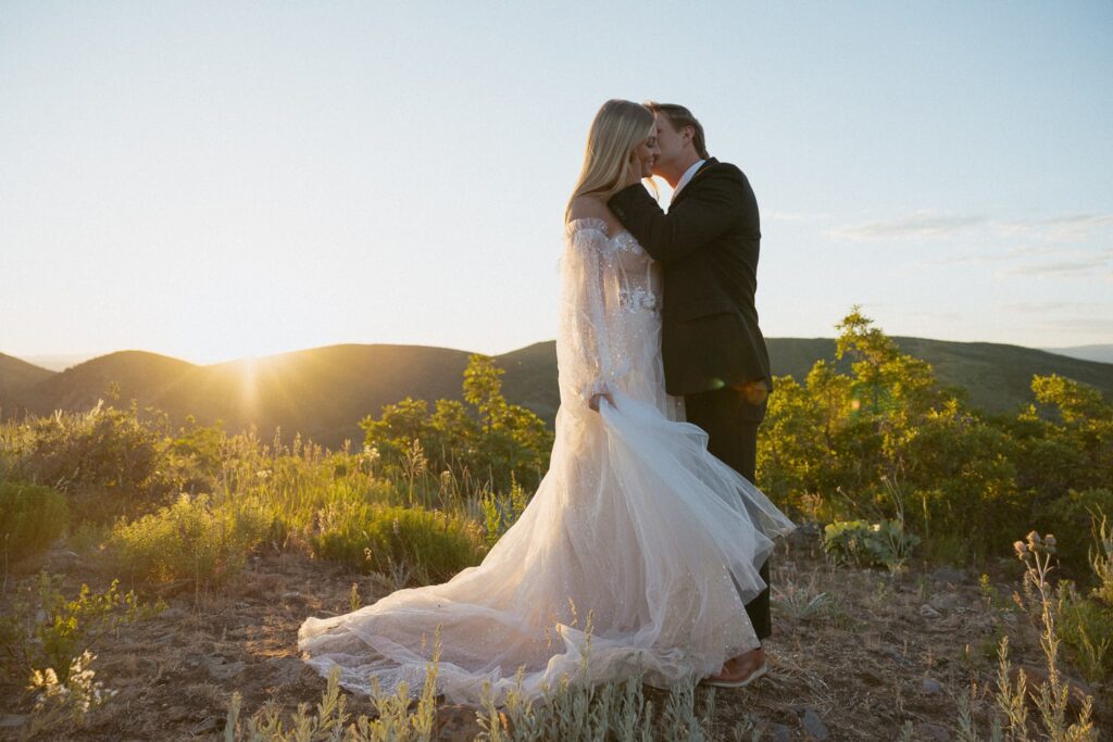 Man whispering in womans ear while in wedding attire with mountains and sunset behind them.