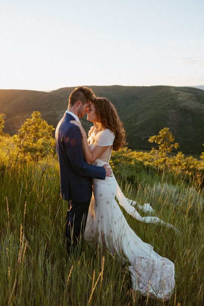 Man and woman standing forehead to forehead while in wedding attire with mountains and sunset behind them.