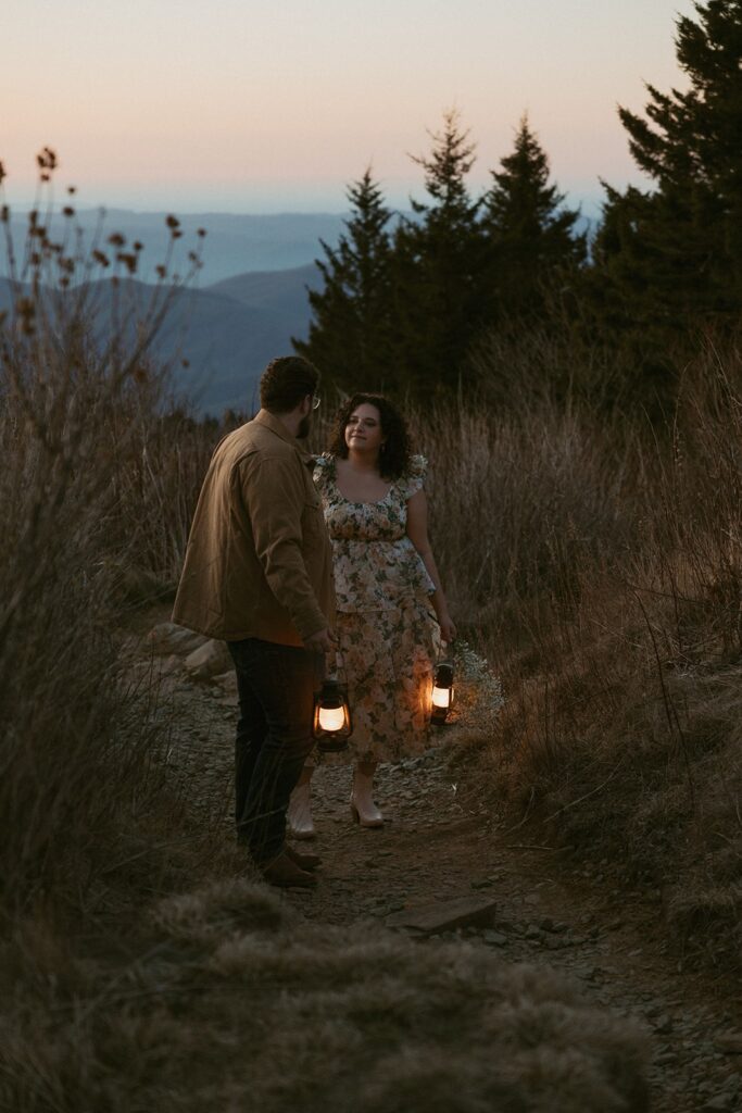 Man and woman standing on a trail looking at each other while holding lanterns at sunrise.