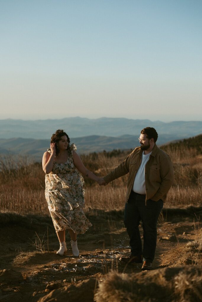 Man and woman holding hands and looking at each other with mountains behind them.