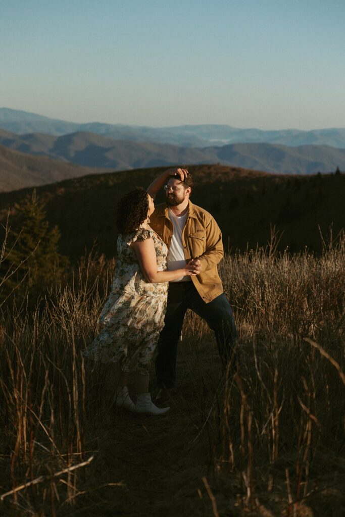 Woman fixing mans hair while standing on a trail with mountains behind them.