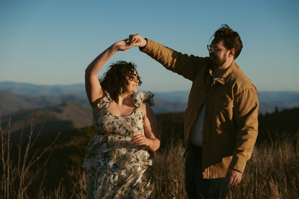 Man spinning a woman by the hand with the mountains behind them.