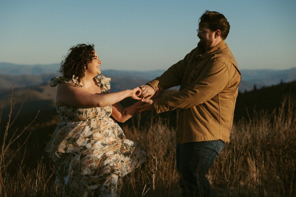 Man and woman laughing and dancing with the mountains behind them.