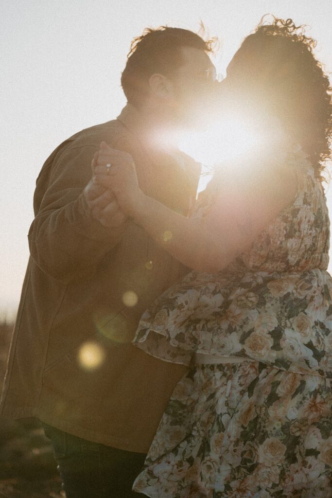 Man and woman holding hands and kissing with the sun shining between them.