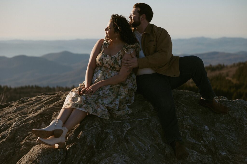 Man and woman sitting on a rock with the mountains behind them.