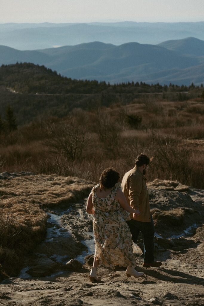 Man leading woman down a hiking trail with mountains behind them.