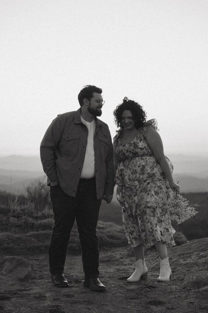 Man and woman holding hands and laughing with mountains behind them.