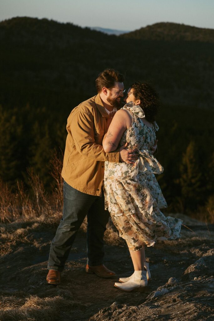 Man and woman smiling and touching noses with mountains behind them.