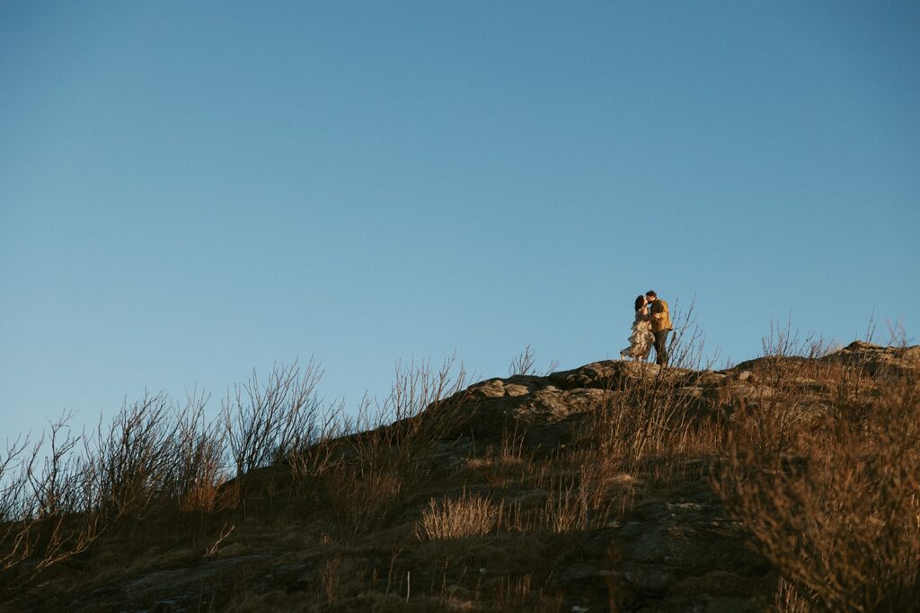 Man and woman standing on top of a mountain with blue sky behind them.