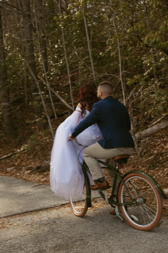 Man and woman in wedding attire riding a bike together.