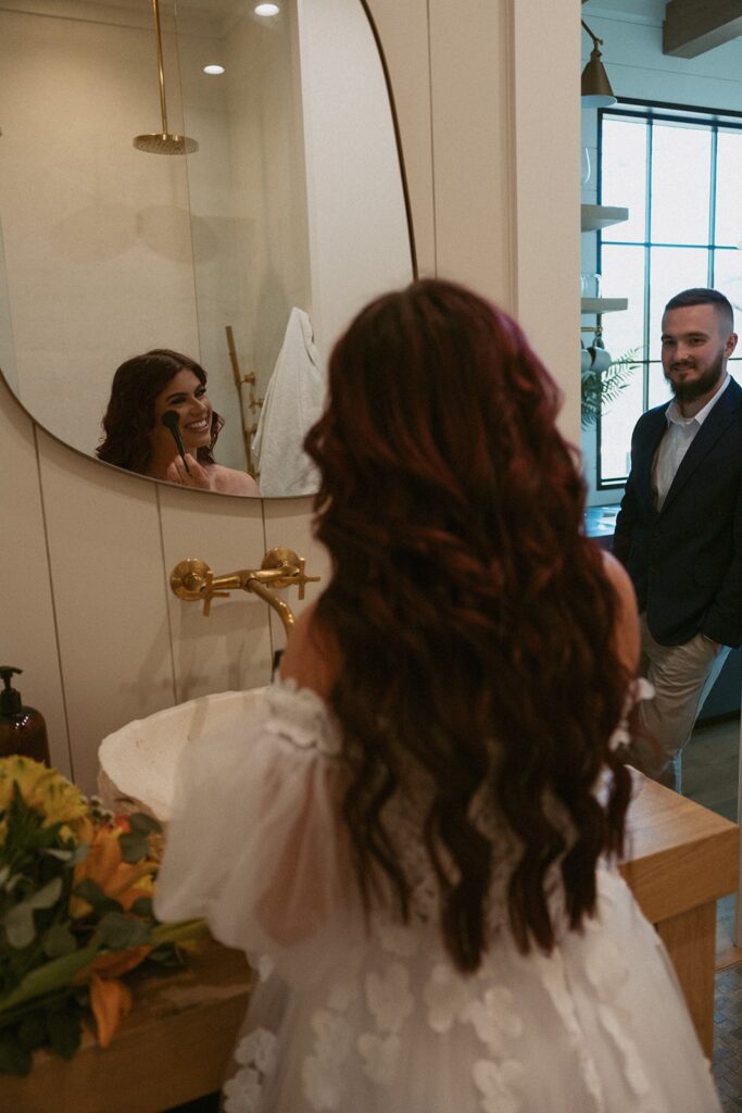 Man watching woman put on makeup in bathroom mirror.