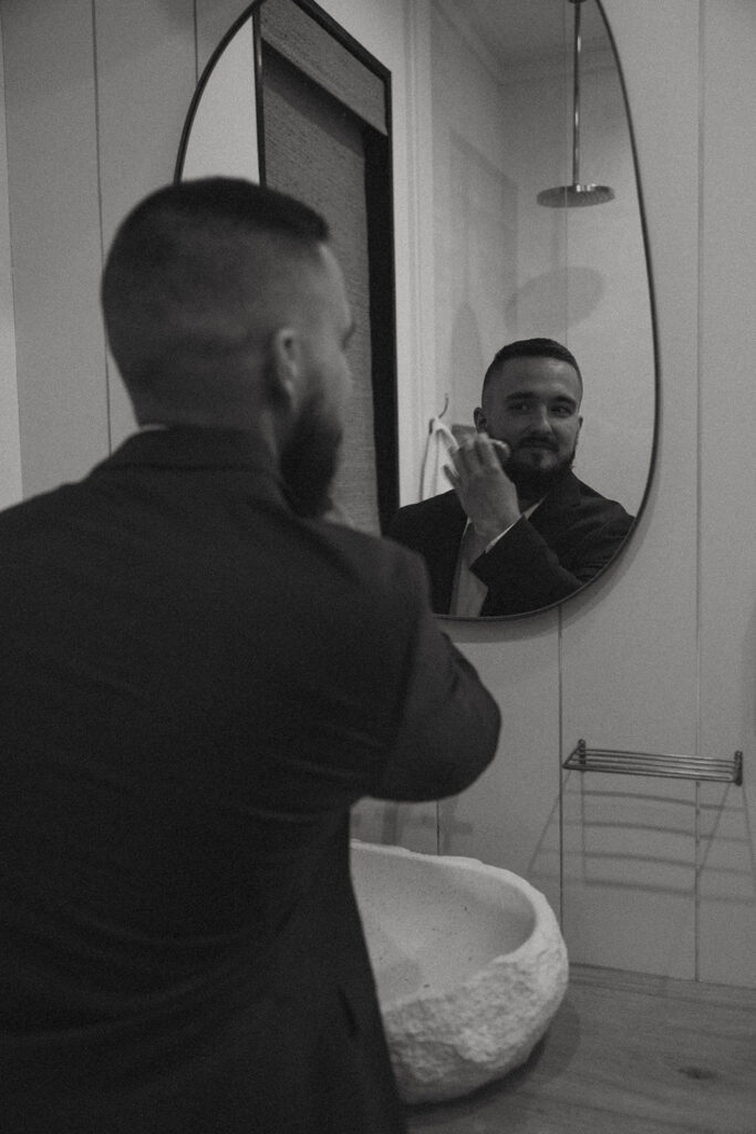 Man brushing his beard in bathroom mirror.