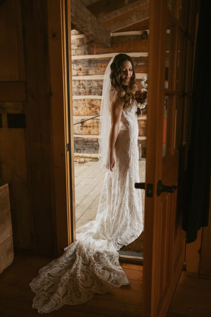 woman in wedding dress walking through doorway of cabin.