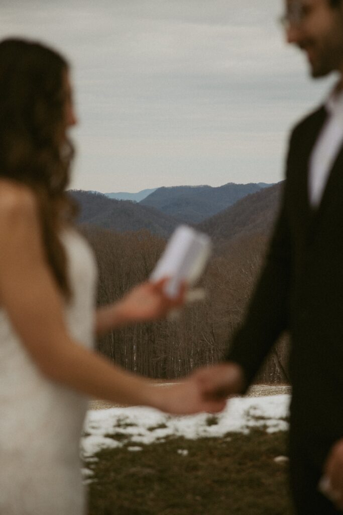 Close up of woman reading vows during elopement with mountains in focus behind them.