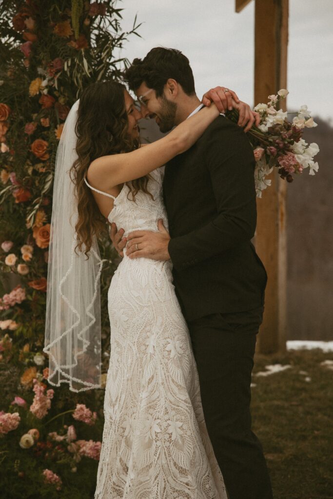 Man and woman in wedding attire hugging and smiling at each other. 