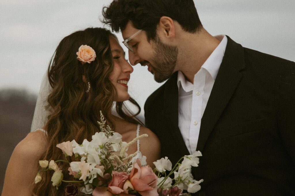 Man and woman with their faces close and smiling at each other with bouquet in foreground.