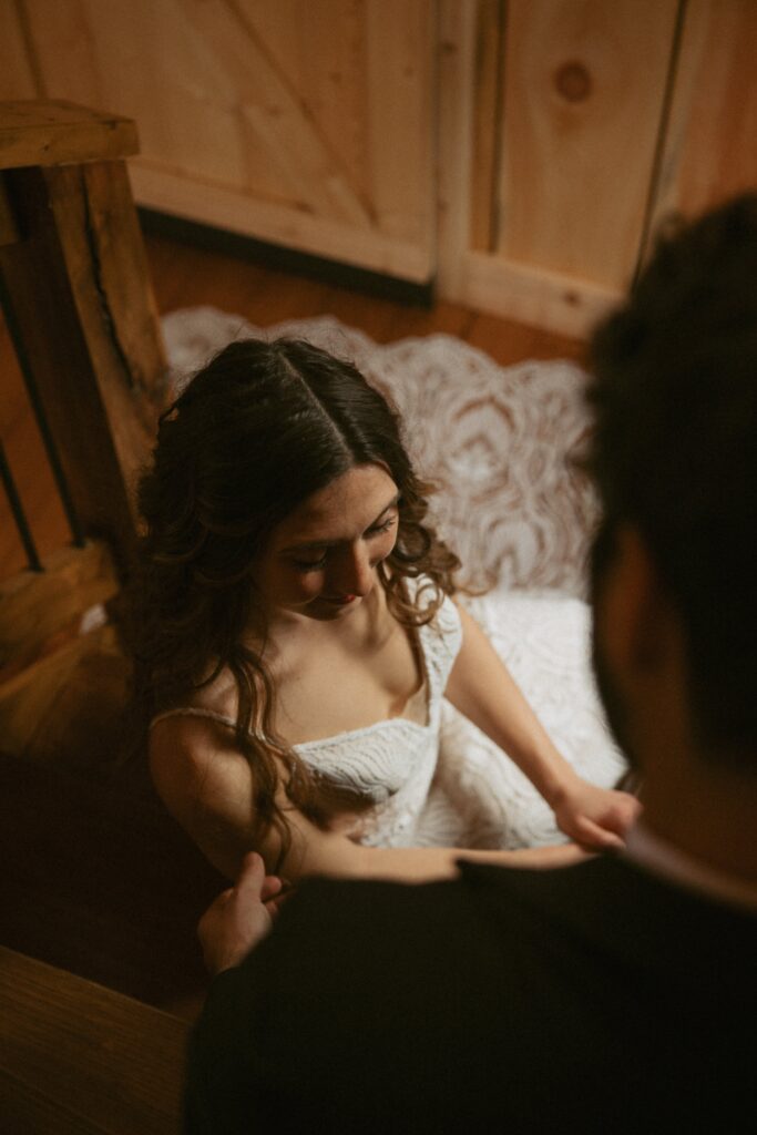 Man and woman in wedding attire sitting on inside stairs with window light shining on them.