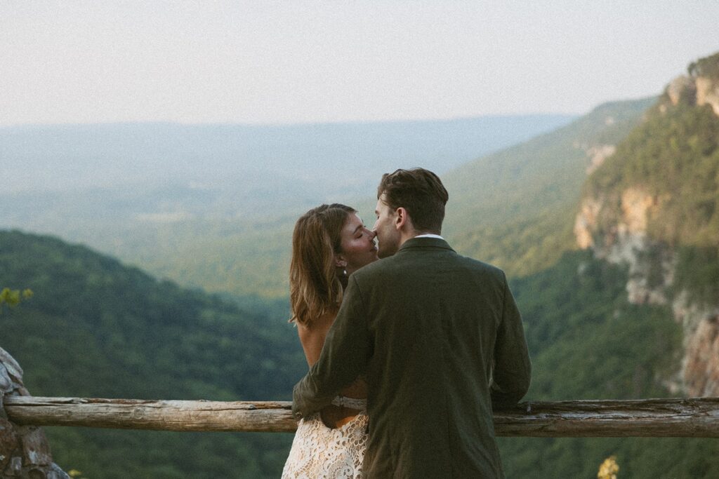 Man and woman in wedding attire going in for a kiss at the main overlook in Cloudland Canyon State park.