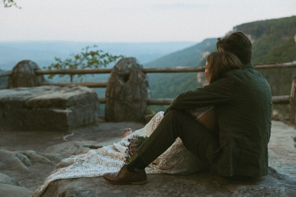 Man and woman in wedding attire sitting on rock at the main overlook in Cloudland Canyon State park.