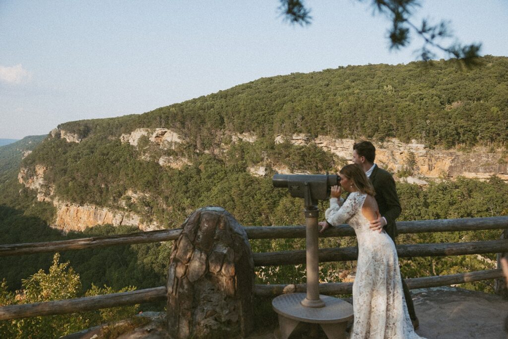 Man and woman in wedding attire looking through viewfinder at the main overlook in Cloudland Canyon State park.