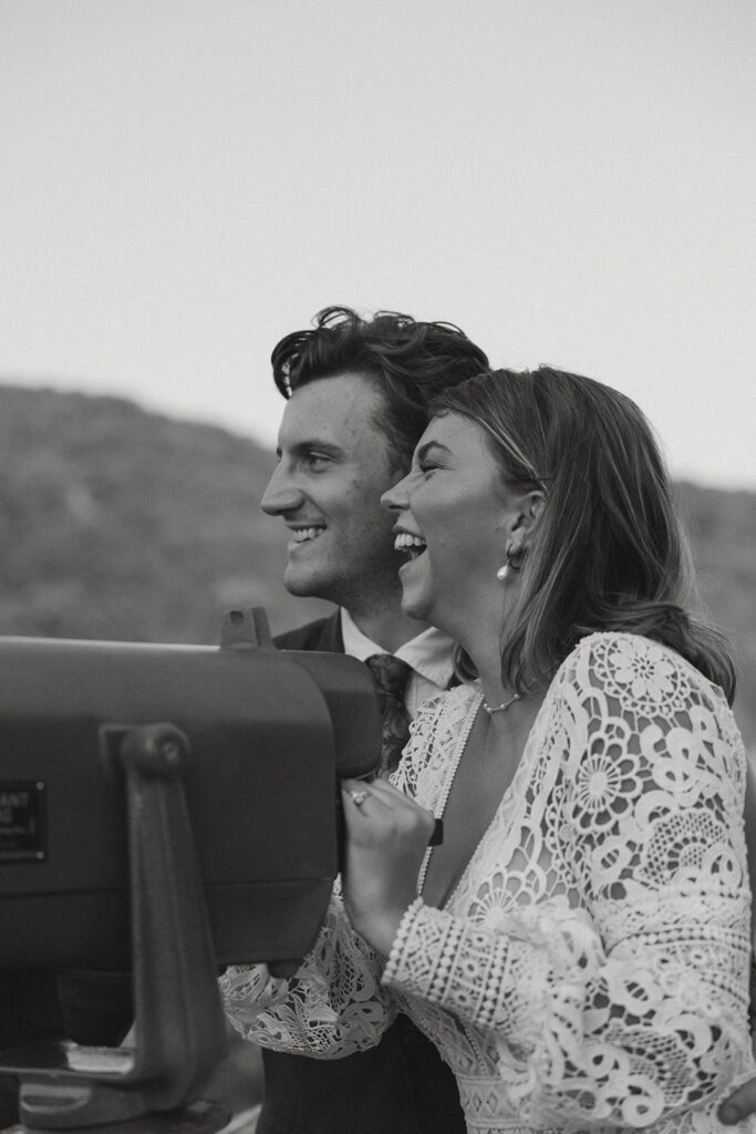 Man and woman in wedding attire laughing and looking through the viewfinder at the main overlook in Cloudland Canyon State park.