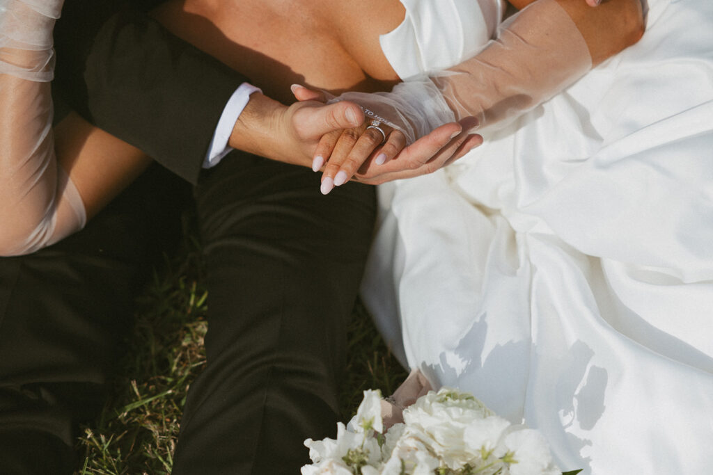 Man and woman sitting and holding hands in wedding attire with the focus on her ring.