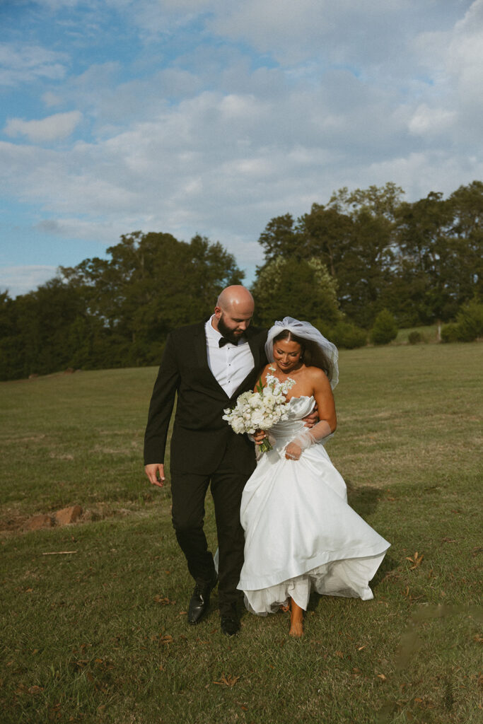 Man and woman in wedding attire walking in open, green field at walker century farms.