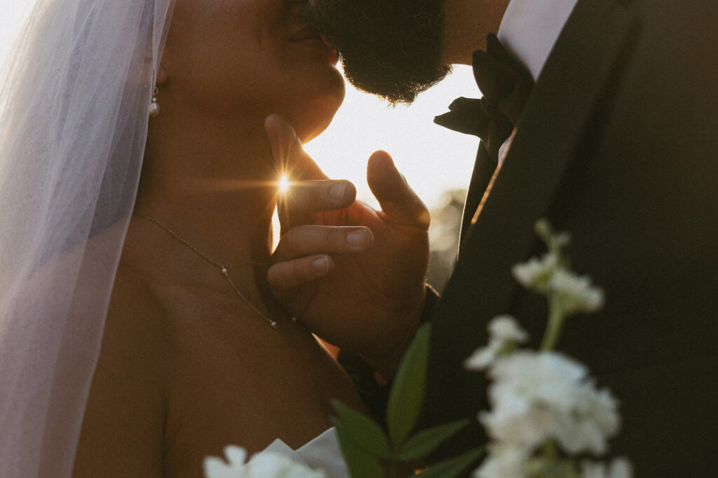 Close up of man and woman going in for a kiss with the sun shining through man's fingers that are on her chin.