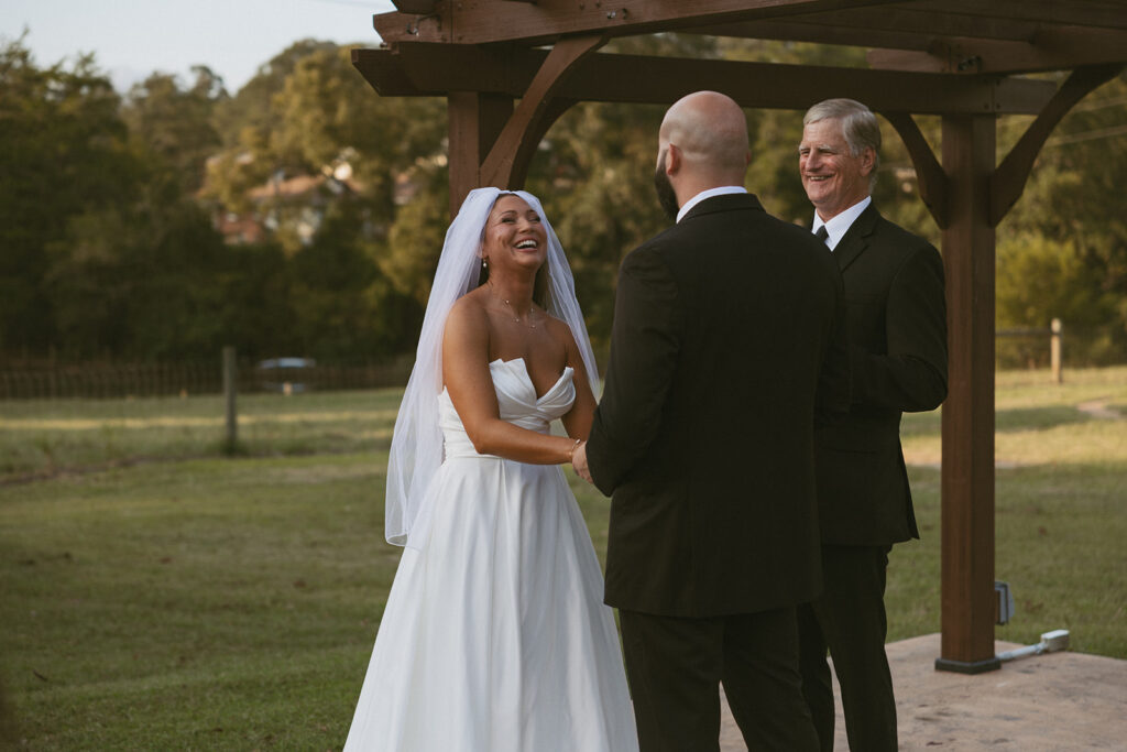 Man and woman laughing and standing in front of officiant during their wedding. 