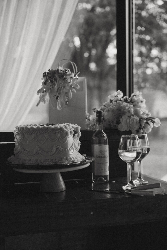 Wine, wine glasses, flowers and small wedding cake at a wedding reception.