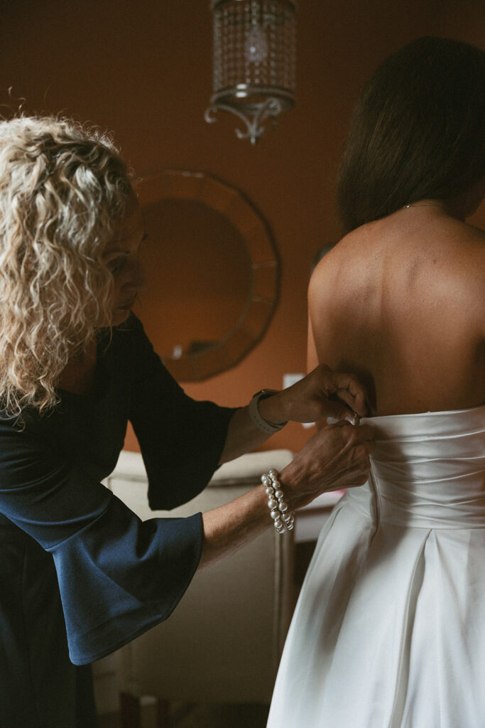 mom helping zip up her daughters wedding dress.