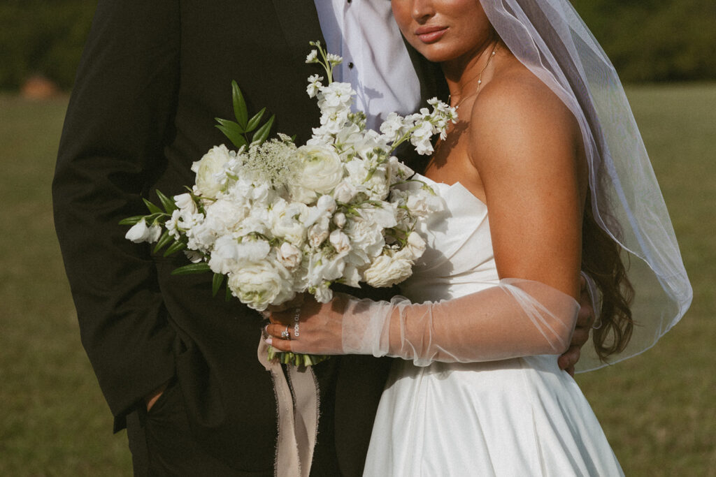 Man and woman in wedding attire standing together with the focus on the bride holding a bouquet. 