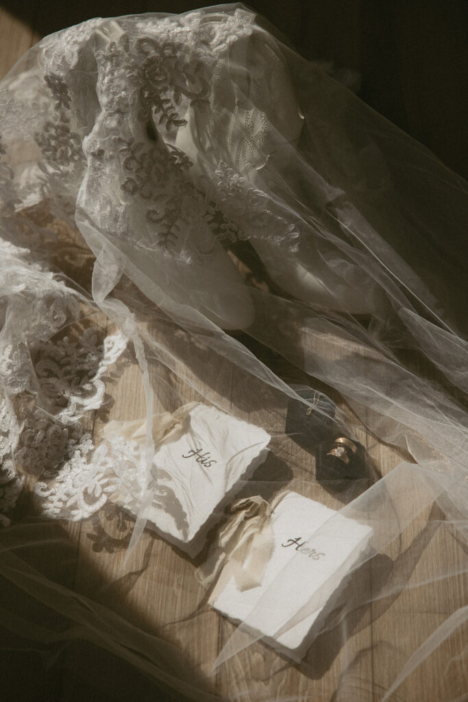 his and hers vow books laying with wedding rings and wedding boots with veil over them