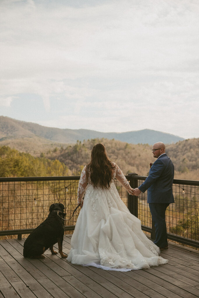 bride and groom standing on airbnb deck with their dog looking at the north georgia mountains during their elopement