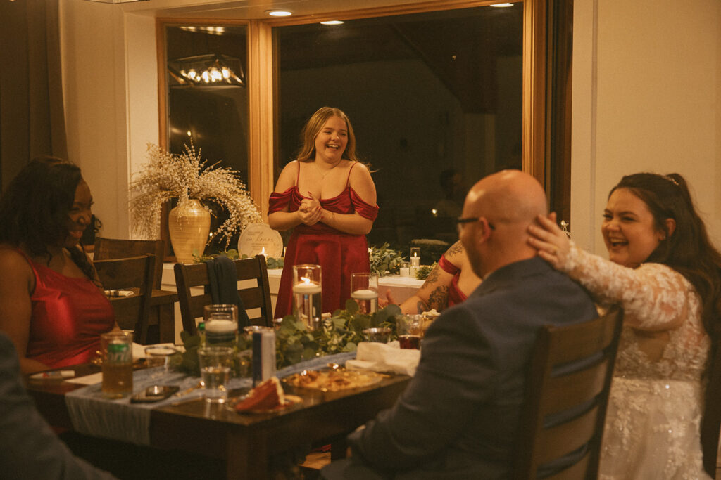 girl giving a toast at wedding reception with bride laughing