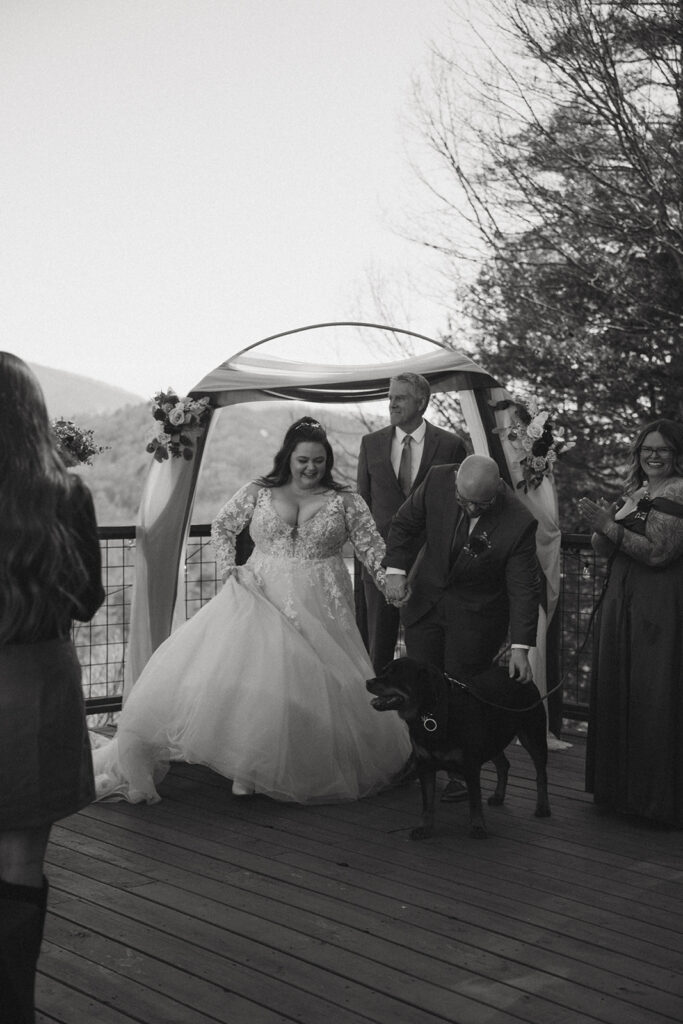 man and woman in wedding attire at alter with their dog and mountains behind them