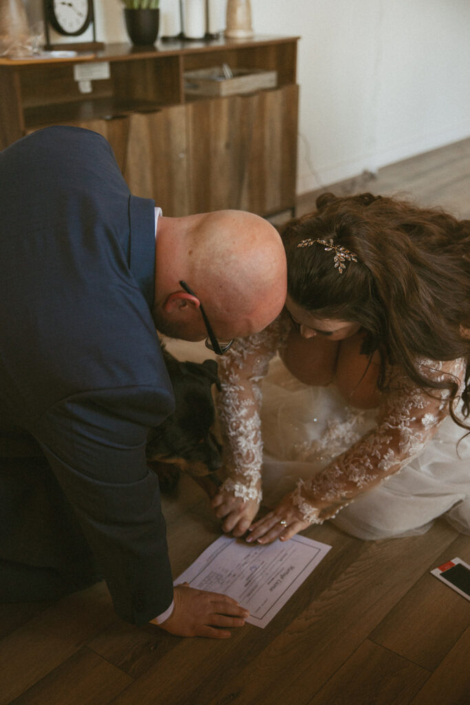 Man and woman in wedding attire helping put there dog's paw print on their marriage license