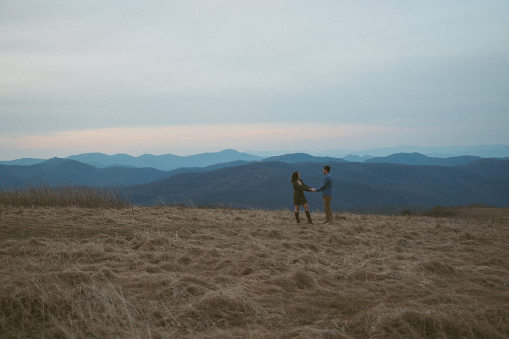 Man and woman holding hands and looking at each other during engagement photos at Max Patch mountain in North Carolina.