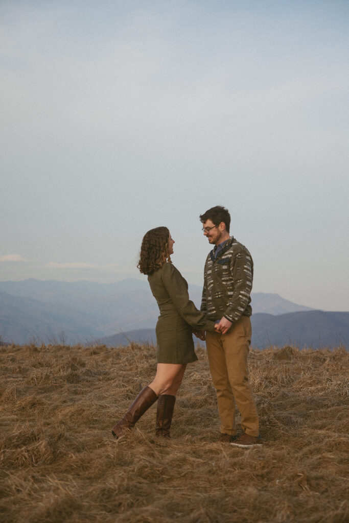 Man and woman holding hands and looking at each other during engagement photos at Max Patch mountain in North Carolina.