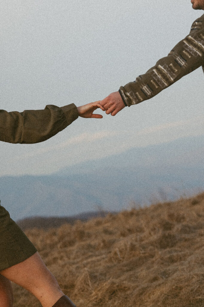Man and woman holding hands during engagement photos at Max Patch mountain in North Carolina.
