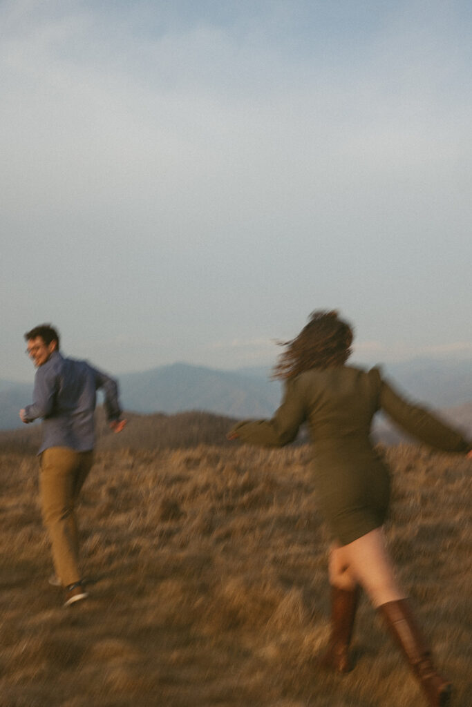 Woman chasing man during engagement photos at Max Patch mountain in North Carolina.